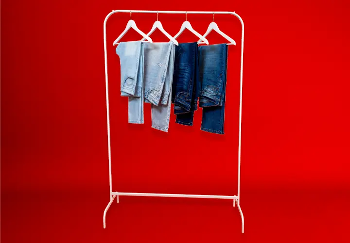 Biały wieszak z czterema parami niebieskich dżinsów wiszącymi na tle intensywnie czerwonym.